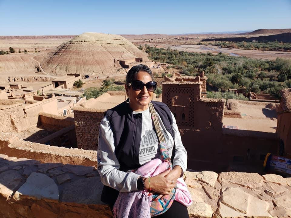 A woman in sunglasses and a vest is sitting on the wall of an old building.