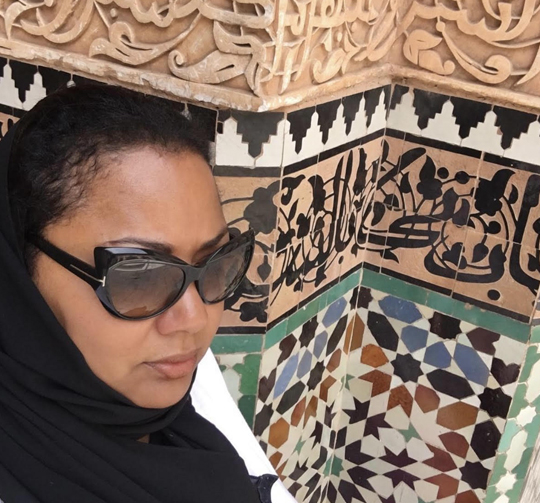 A woman wearing sunglasses and standing in front of a wall.